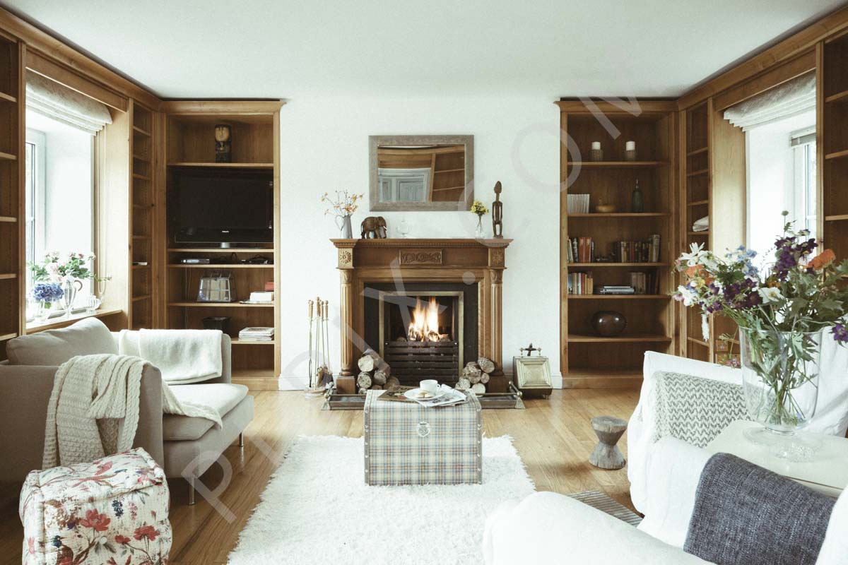 Livingroom with timber flooring rug timber bookshelves fireplace sofa mirror trunk table flowers foot stools